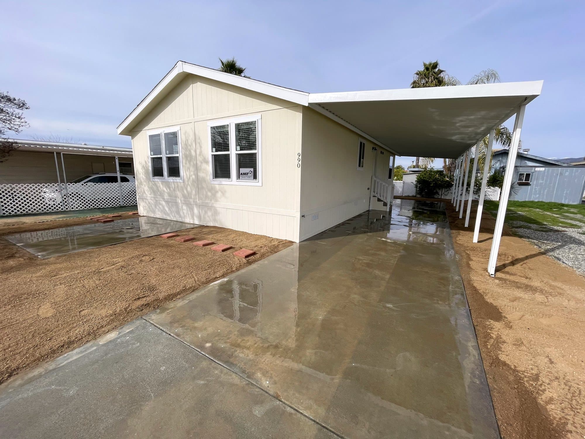 Cream manufactured home with a white awning over a wet concrete pad