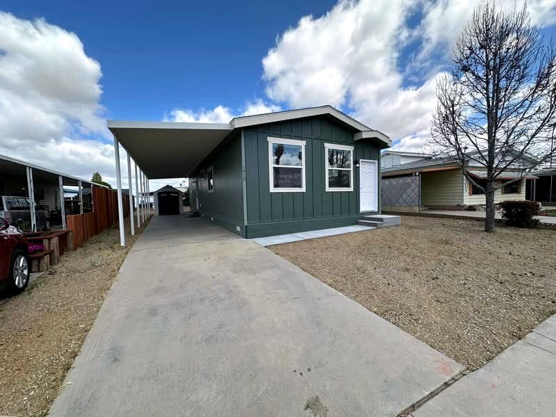 Sage green manufactured home with a metal carport and white door